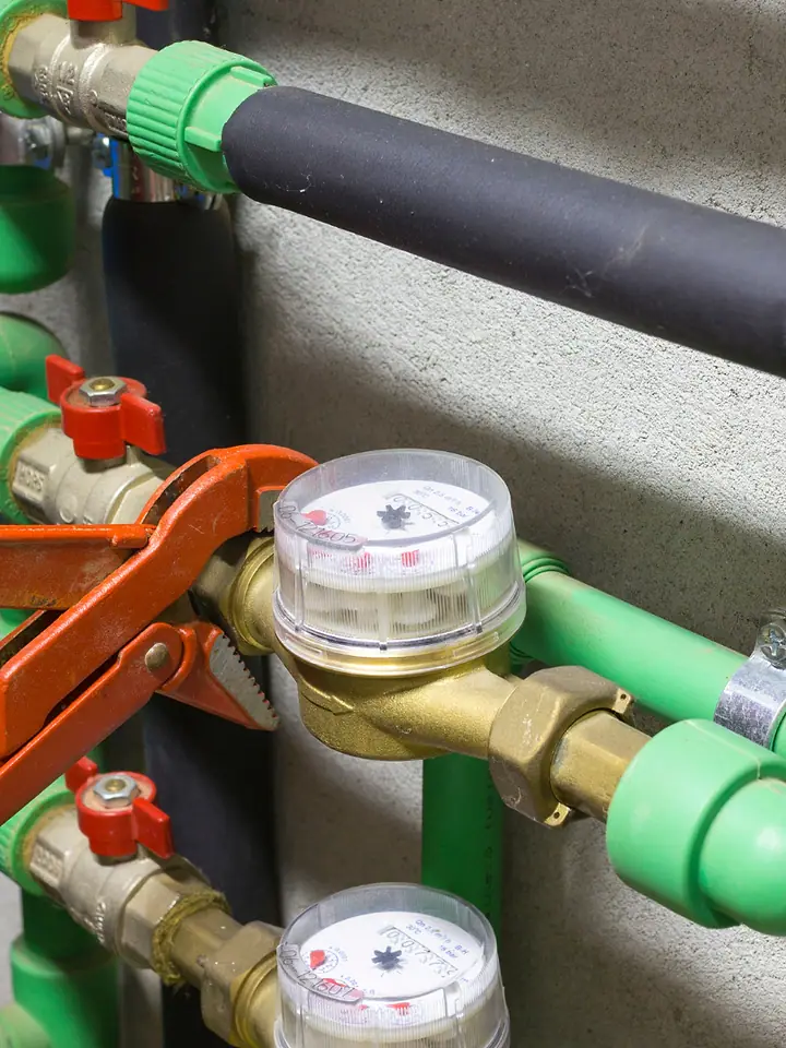 Mão apertando com chave de grifo a conexão de um hidrômetro na tubulação verde